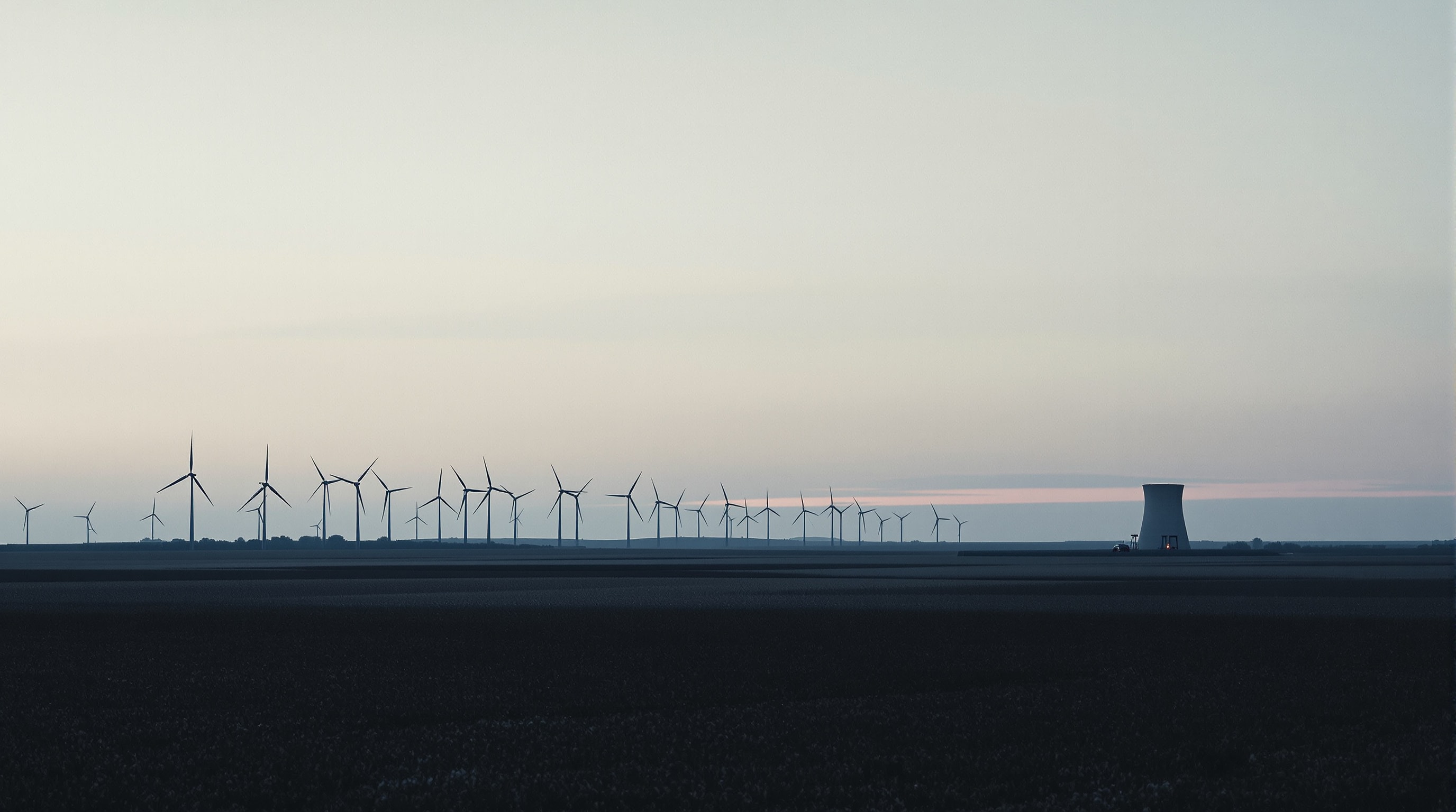 Wind turbines and a cooling tower seen together across flat farmland at dusk